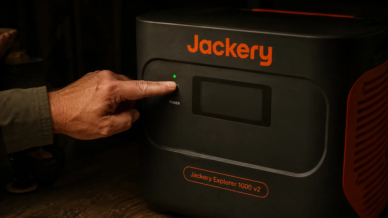 Hand pressing the power button on the Jackery Explorer 1000 v2 in a dark room
