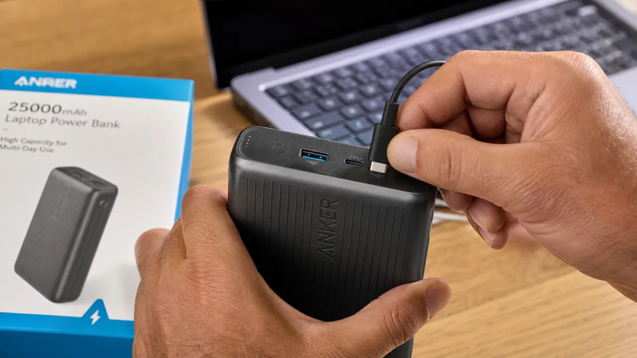 USB-C cable plugged into the side of a power bank, laptop visible in background