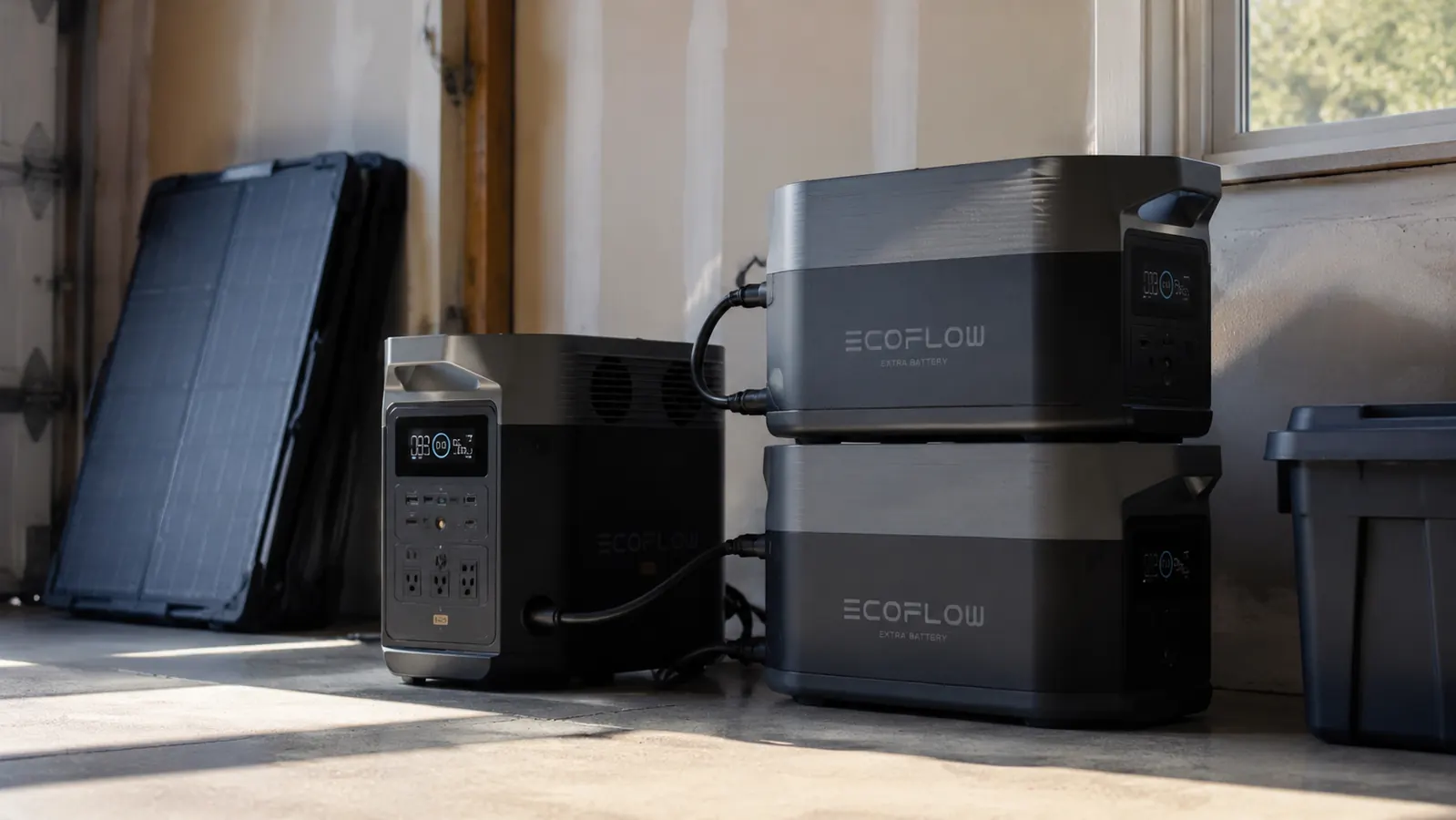 Two EcoFlow Extra Batteries stacked beside a Delta Pro with a solar panel visible through a garage window