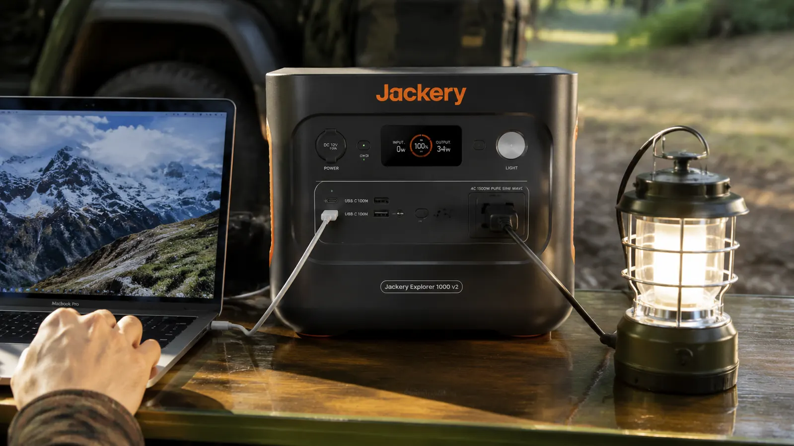 Jackery Explorer 1000 v2 front panel showing AC outlets and USB-C ports being used simultaneously to charge a laptop and a camping lantern