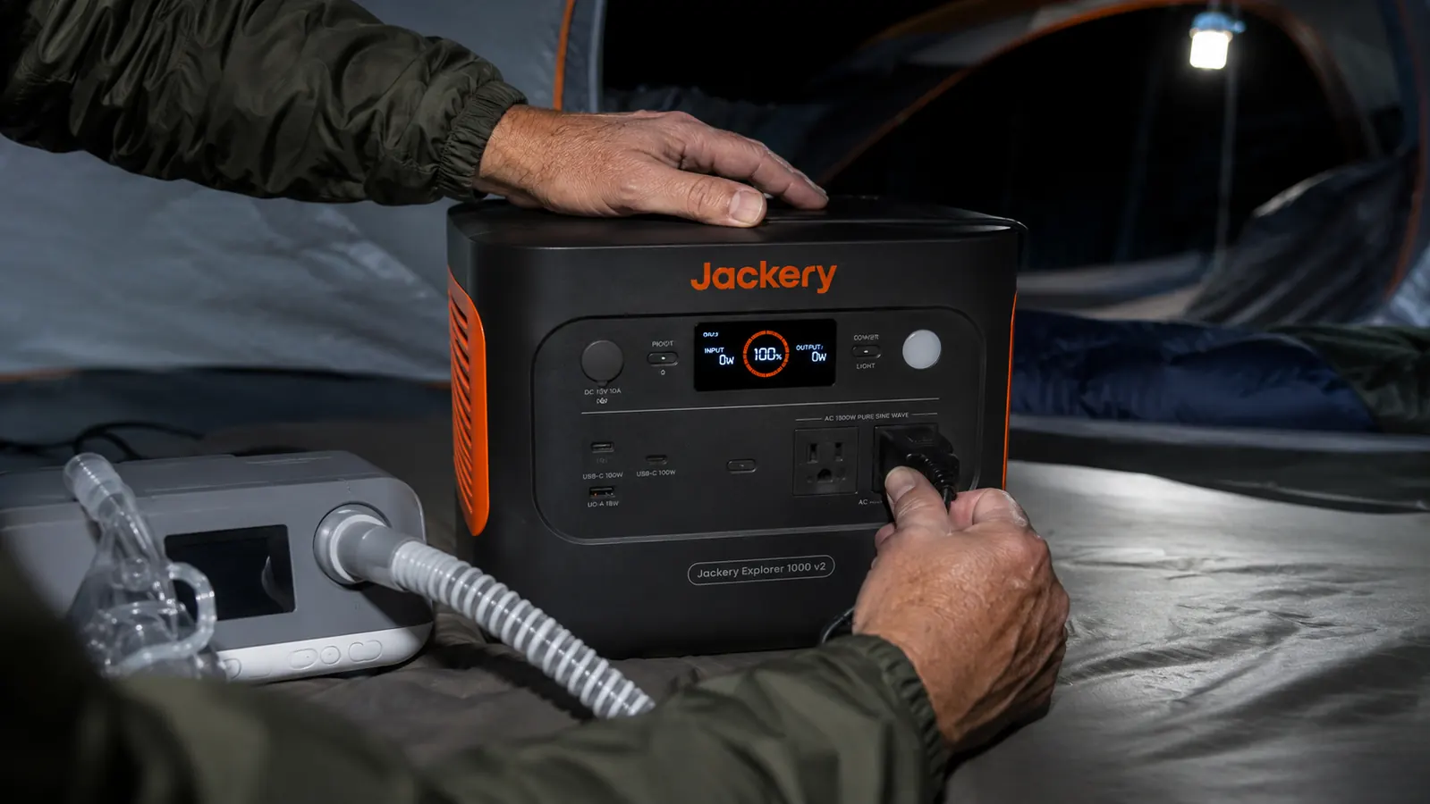 Man plugging a CPAP machine power cord into a Jackery Explorer 1000 v2 portable power station in a tent