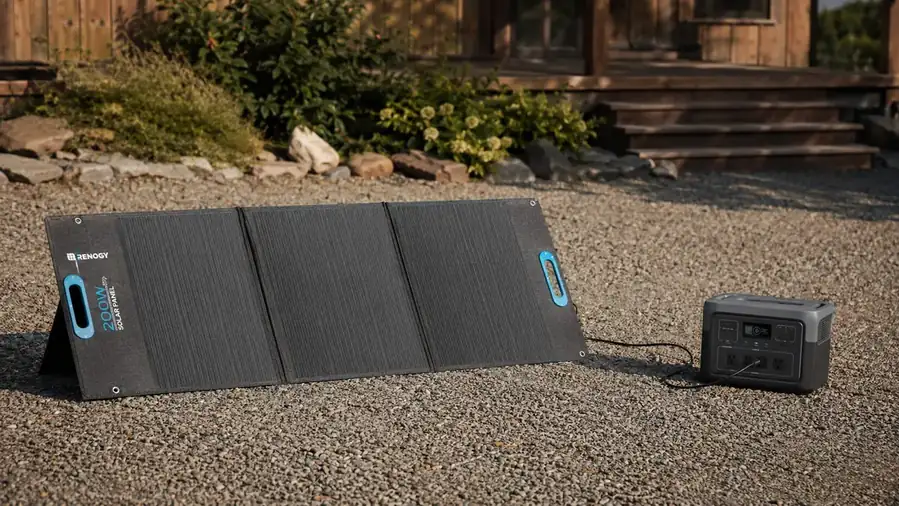 Renogy 200W foldable solar panel deployed on gravel beside a power station with an MC4 cable running between them